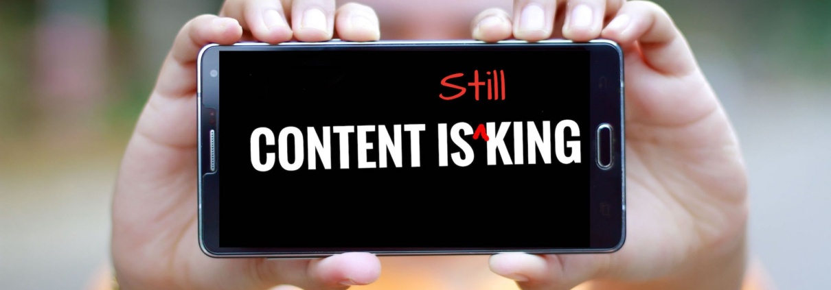 A woman in yellow holds up a cellphone with 'Content is King' on the screen. In red, the word "still" has been added, so that the text reads "content is still king"